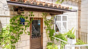 Un edificio con techo de tejas, puerta de madera y balcón con plantas en macetas.