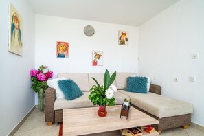 A living room with a sofa, coffee table, and artwork on the wall. - Apartments & Rooms Mara & Petrunjela - One Bedroom Apartment with Garden (Cavtat)