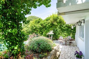 A patio with stone flooring, a table with chairs, and a white building with windows. - Apartments & Rooms Mara & Petrunjela - One Bedroom Apartment with Garden (Cavtat)