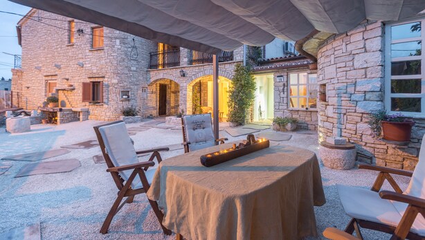 An outdoor patio area with stone walls, a table with a tablecloth, and several chairs.