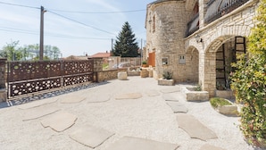 A courtyard with stone pathways, a stone building with a balcony, and a metal fence.