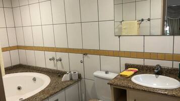 A bathroom with a bathtub, a sink, and a toilet. There are towels and toilet paper on the counter.