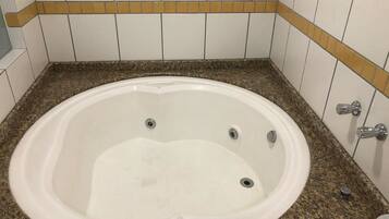 A bathroom with a white bathtub, granite countertop, and white tiled walls with a yellow border.