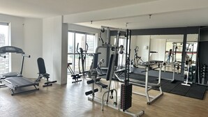 Un gimnasio espacioso con diversos equipos de ejercicio, ventanas amplias y un espejo que refleja el espacio.