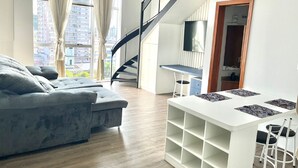 Una sala de estar moderna con un sofá gris, una mesa de centro blanca y una escalera que sube a un nivel superior.