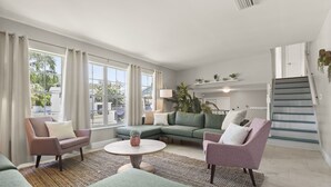 Uma sala de estar moderna com um sofá de canto, poltronas, uma mesa de centro e uma escada.