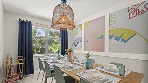 Uma sala de jantar com mesa de madeira posta para quatro, cadeiras, luminária pendente e obras de arte na parede.