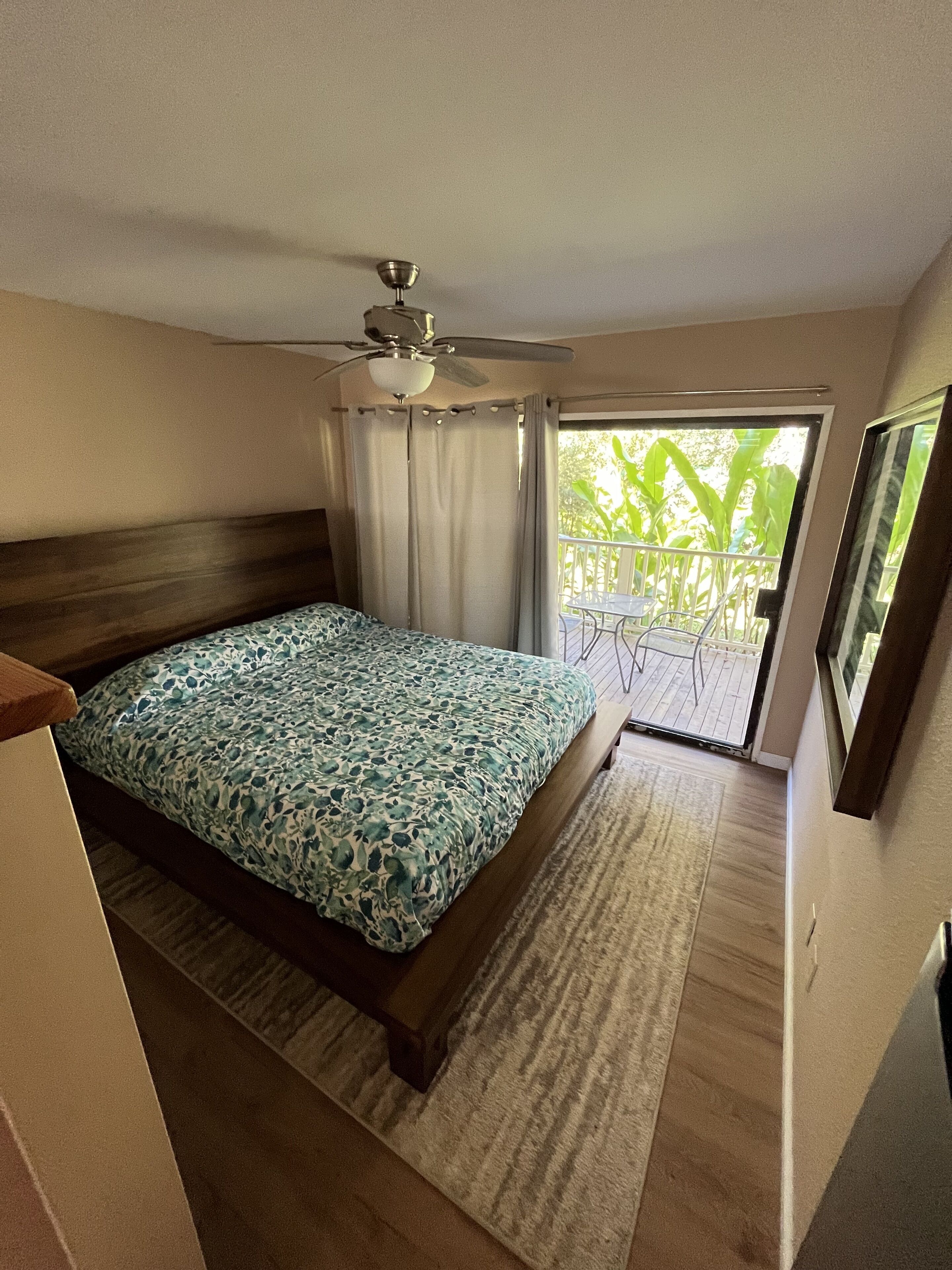 A bedroom with a bed, a ceiling fan, a view of the outdoors, and a balcony.