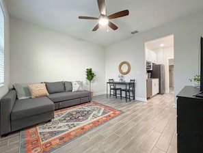 A modern living room with a gray sofa, a patterned rug, a ceiling fan, and a dining area with chairs and a table. - Brand new private suite near Disney and Universal! (Ocoee)