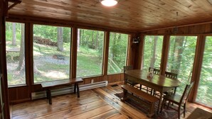 A wooden cabin with a large dining table and benches, large windows offering a view of the forest. - Treetops Cabin in the Woods! (Bloomingdale)