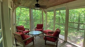 A covered outdoor seating area with wooden furniture and large windows. - Treetops Cabin in the Woods! (Bloomingdale)