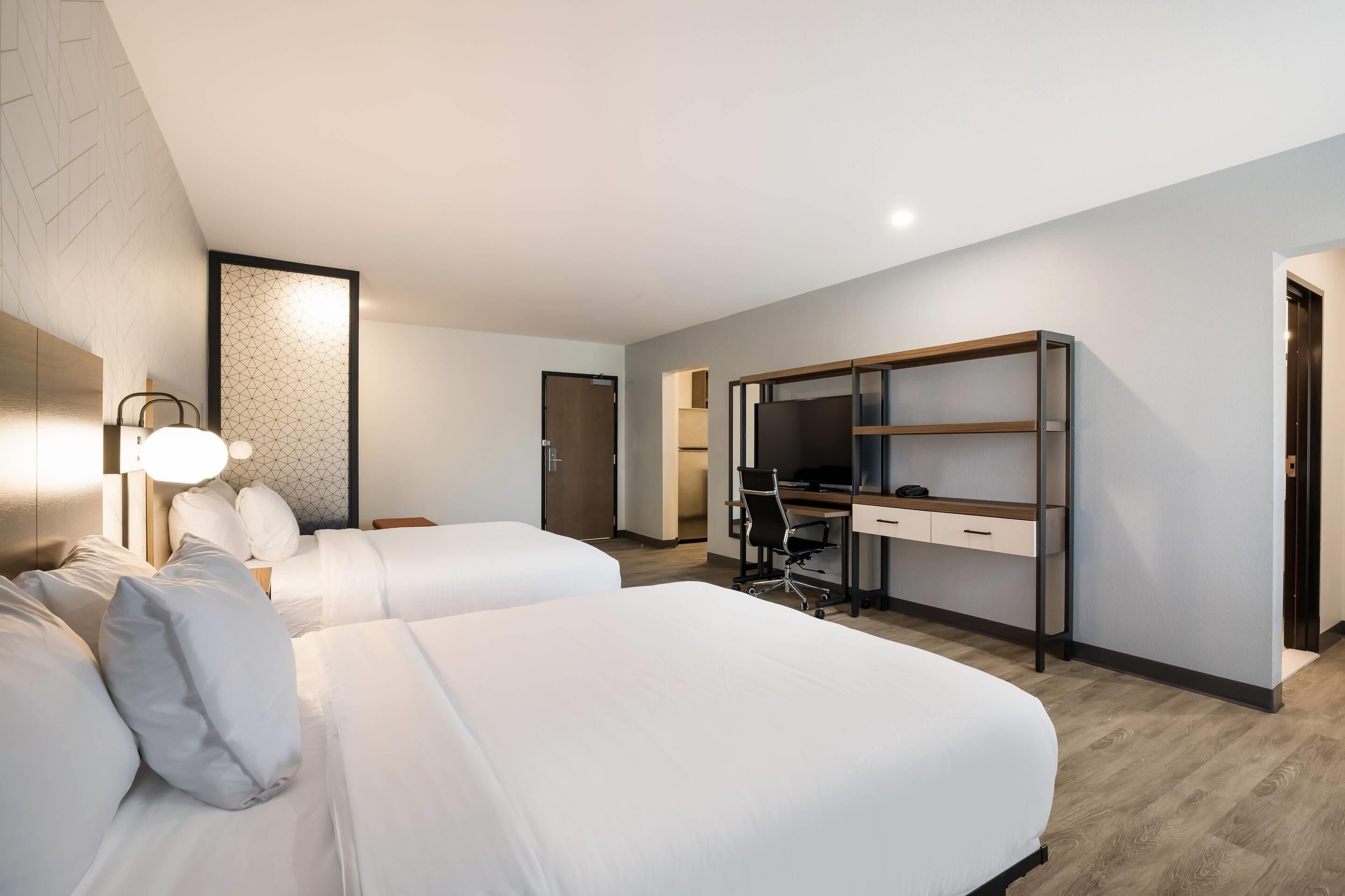 Habitación de hotel con dos camas, un escritorio, una silla y un armario.