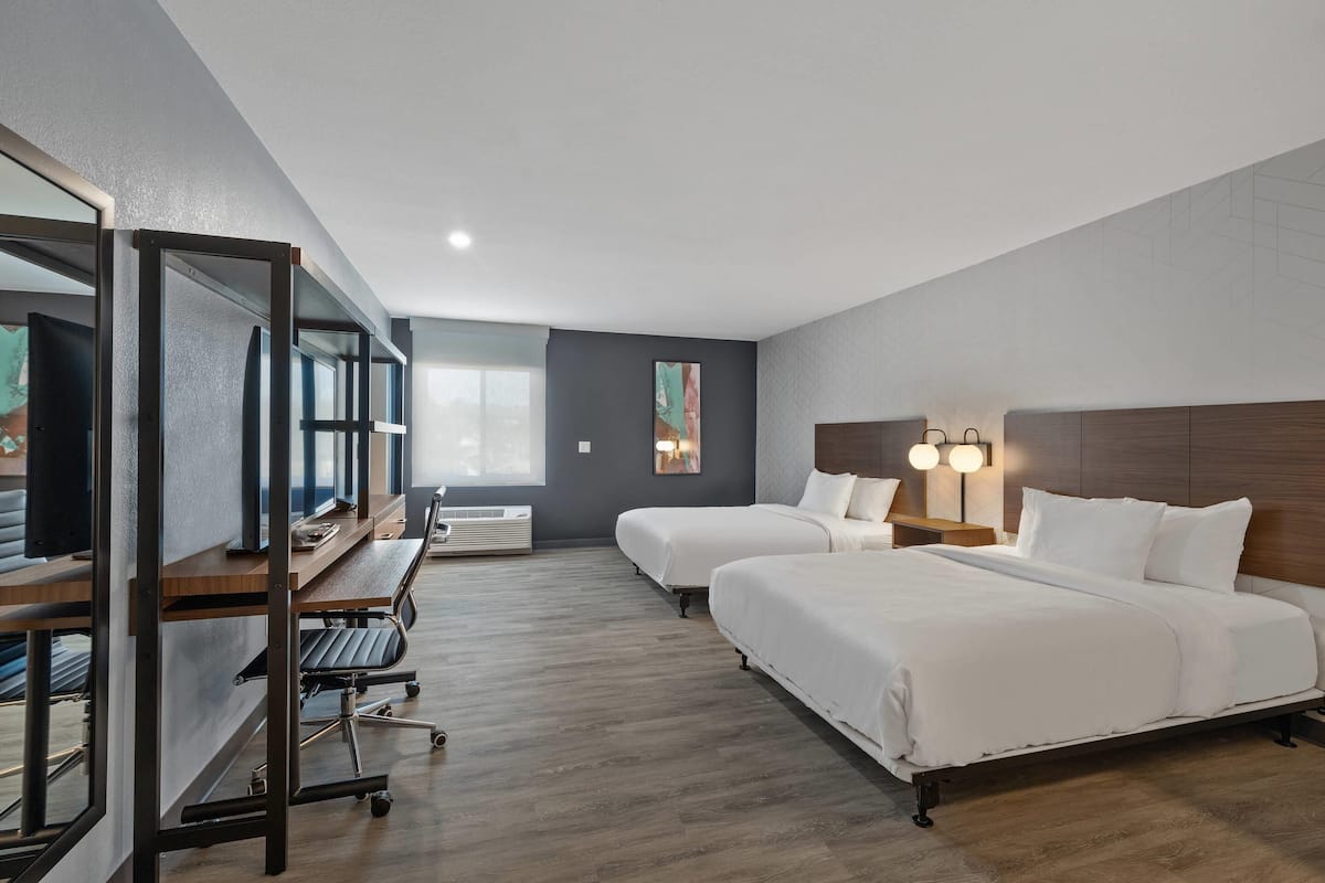A hotel room with two beds, a desk with a computer, and a large window.