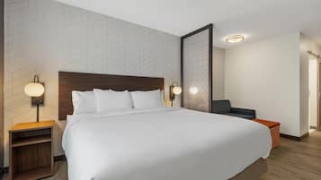 Une chambre d’hôtel moderne avec un grand lit, deux tables de chevet avec des lampes, une tête de lit en bois et un mur orné d’un motif géométrique.