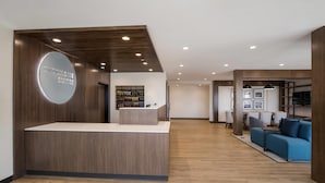 A reception area with a wooden reception desk, a circular sign, and a seating area with sofas and a coffee table. - Everhome Suites Corona (Corona)