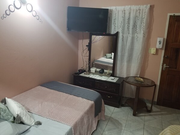 Un dormitorio con cama, cómoda, espejo, televisor y una pequeña mesa.