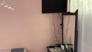 Een slaapkamer met een bed, een dressoir, een aan de muur bevestigde televisie en een klein tafeltje met decoratieve objecten.