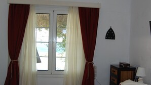 A bedroom with a bed, a ceiling fan, a window with curtains, a nightstand, and a lamp.