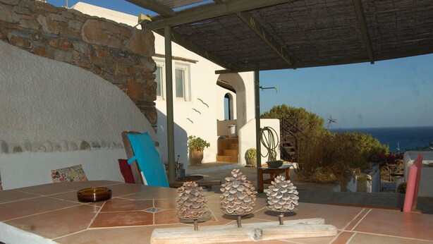 A patio with a stone wall, a covered area, and a view of the sea.