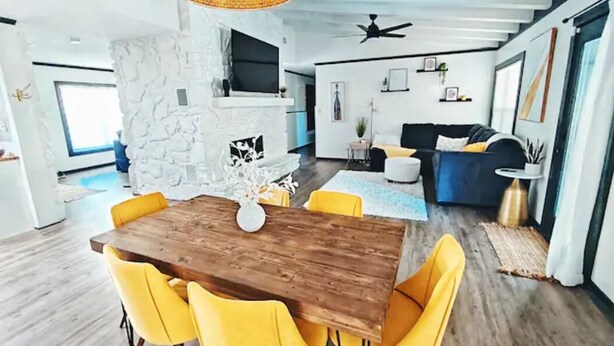 A modern living room with a wooden dining table and yellow chairs, a stone fireplace, and a blue sofa. - Maison Modernè Unit A: Work + Play (San Antonio)