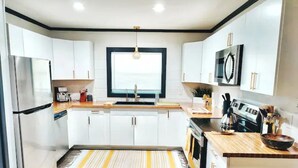 A modern kitchen with white cabinets, a stainless steel refrigerator, a microwave, and a wooden countertop. - Maison Modernè Unit A: Work + Play (San Antonio)