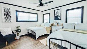 A bedroom with two beds, a ceiling fan, large windows, and a wall art piece. - Maison Modernè Unit A: Work + Play (San Antonio)