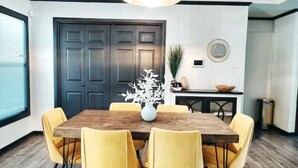 A dining area with a wooden table, yellow chairs, and a vase with white flowers. - Maison Modernè Unit A: Work + Play (San Antonio)