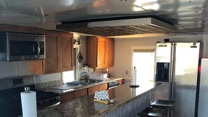 A modern kitchen with a granite countertop, stainless steel appliances, wooden stools, and a birthday cake on the counter. - Rougaroux Lodge @Venice Marina is a Sportsman dream! (Venice)