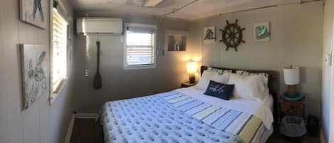 Un dormitorio con cama, un timón de barco en la pared, una ventana con persianas y un aire acondicionado de pared.