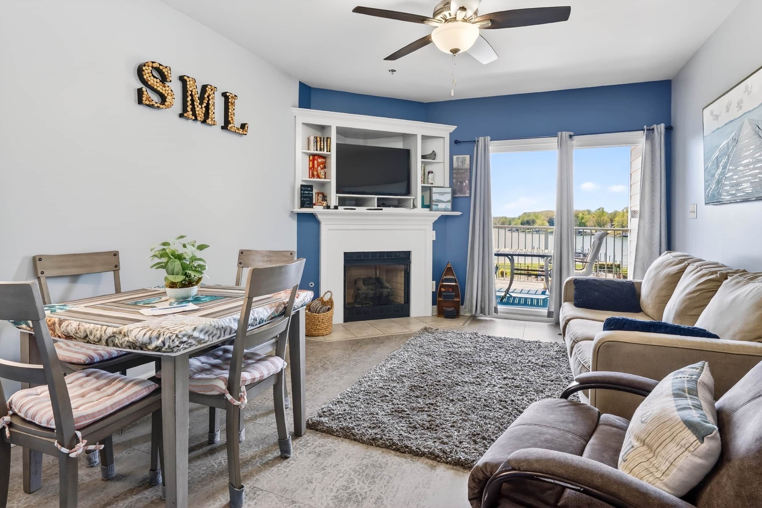A living room with a fireplace, a dining table, chairs, a sofa, and a ceiling fan.