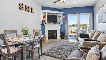 A living room with a fireplace, a dining table, chairs, a sofa, and a ceiling fan.