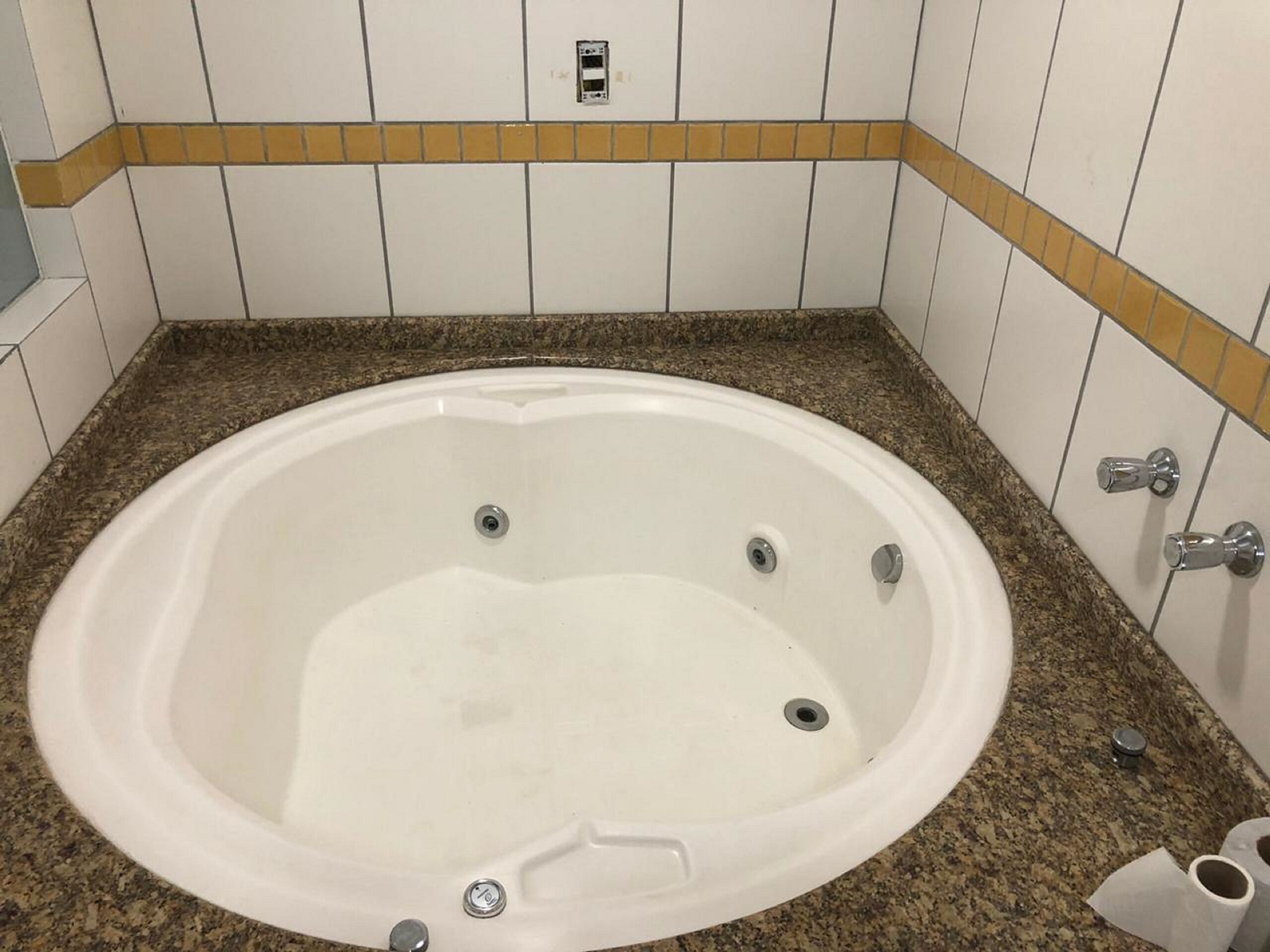Un baño con bañera blanca, encimera de granito y un borde de azulejos amarillos.
