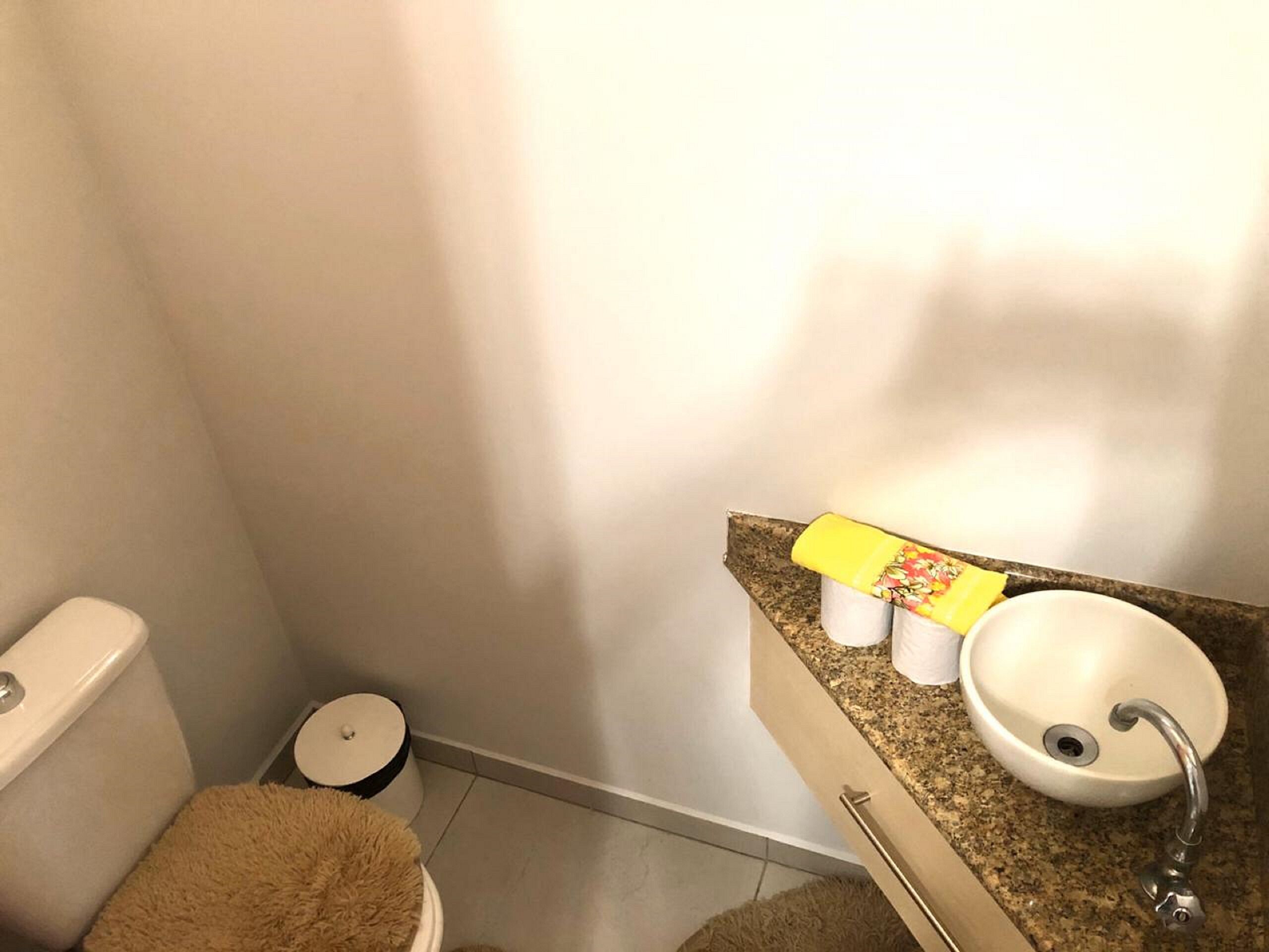 A bathroom with a toilet, a small trash bin, a sink with a faucet, and a towel on the floor.