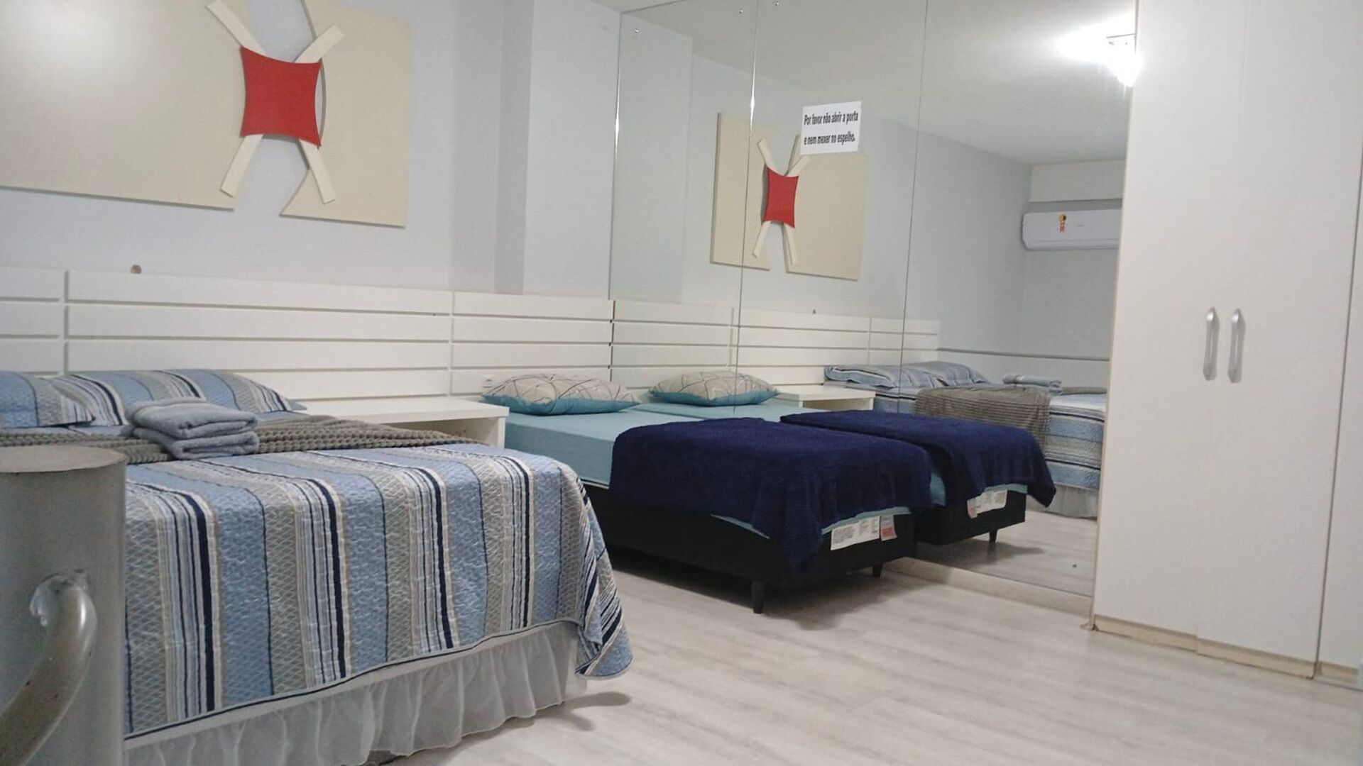 Habitación de hotel con tres camas, un espejo grande y un armario.