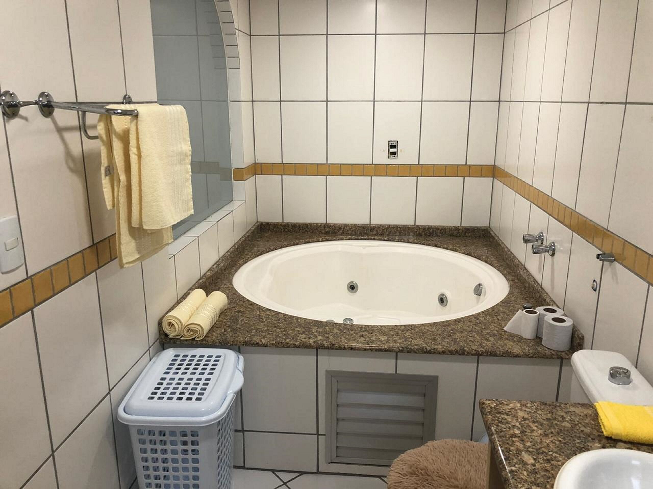 Un baño con bañera, un perchero, un cesto de ropa y un inodoro.