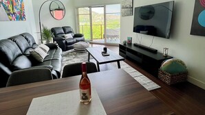 A modern living room with a dining table, leather sofa, TV, and artwork. - Peaceful Retreat with Breathtaking View (West Kelowna)