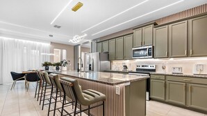 A modern kitchen with a central island, bar stools, and built-in appliances. - 6BR house sleeps 16 with private pool (Kissimmee)