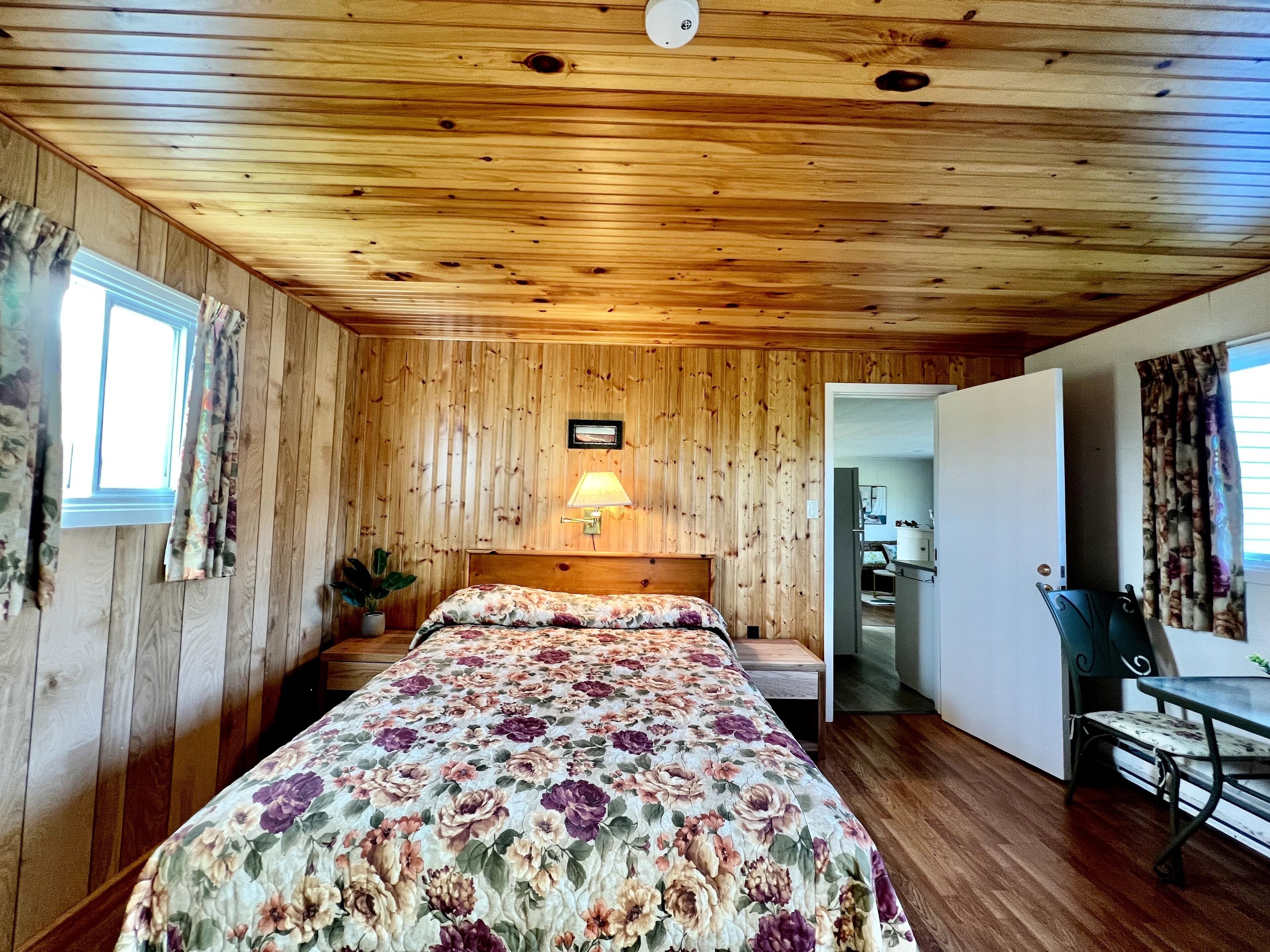 A wooden-paneled room with a bed, a desk, and a lamp.