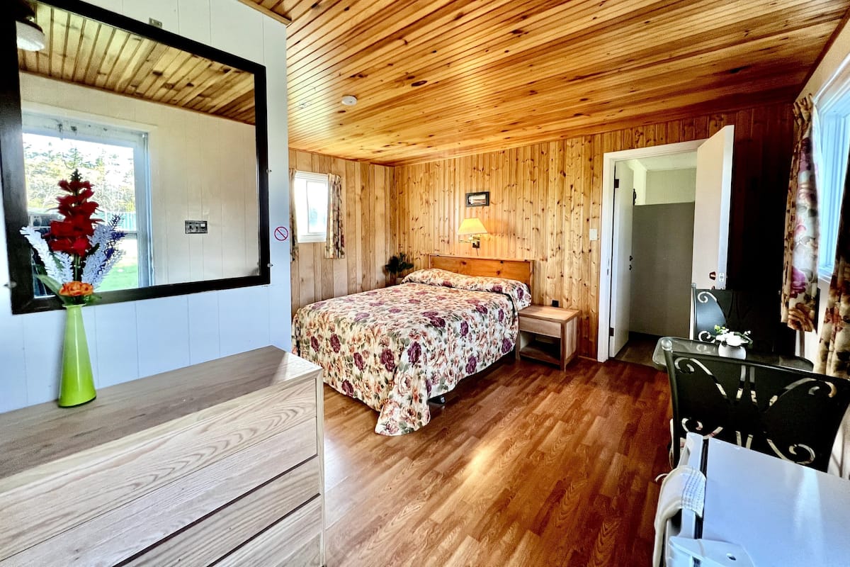 A wooden-paneled room with a bed, bedside table, and a mirror.