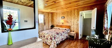 A wooden-paneled room with a bed, bedside table, and a mirror.