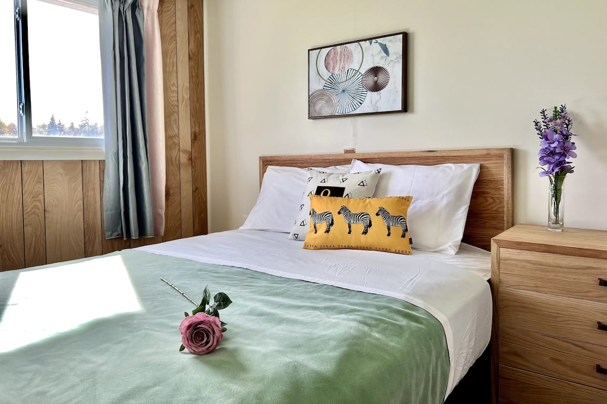 A neatly made bed with a green bedspread, a single rose decoration, and a zebra-themed pillow.