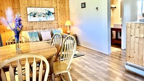A dining area with a wooden table and chairs, a sofa with patterned cushions, a wall-mounted abstract painting, and a wooden cabinet with a built-in heater. - St Lawrence Motel (North Rustico)