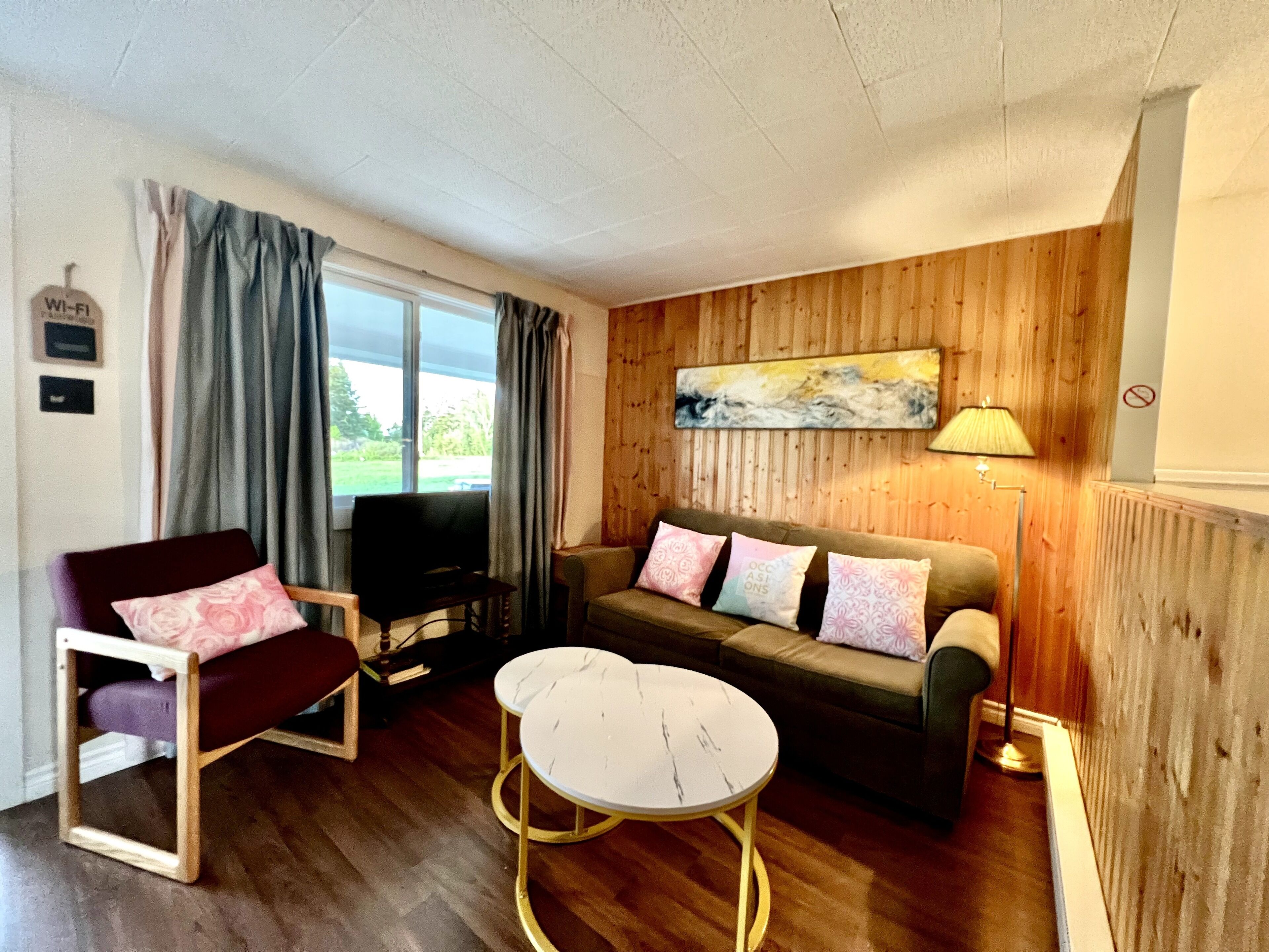 A living room with a wooden floor, a sofa with patterned cushions, a television, and a lamp.