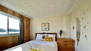 A bedroom with a wooden headboard, a bed with white bedding and decorative pillows, a nightstand with a vase of flowers, and a window with curtains. - St Lawrence Motel (North Rustico)