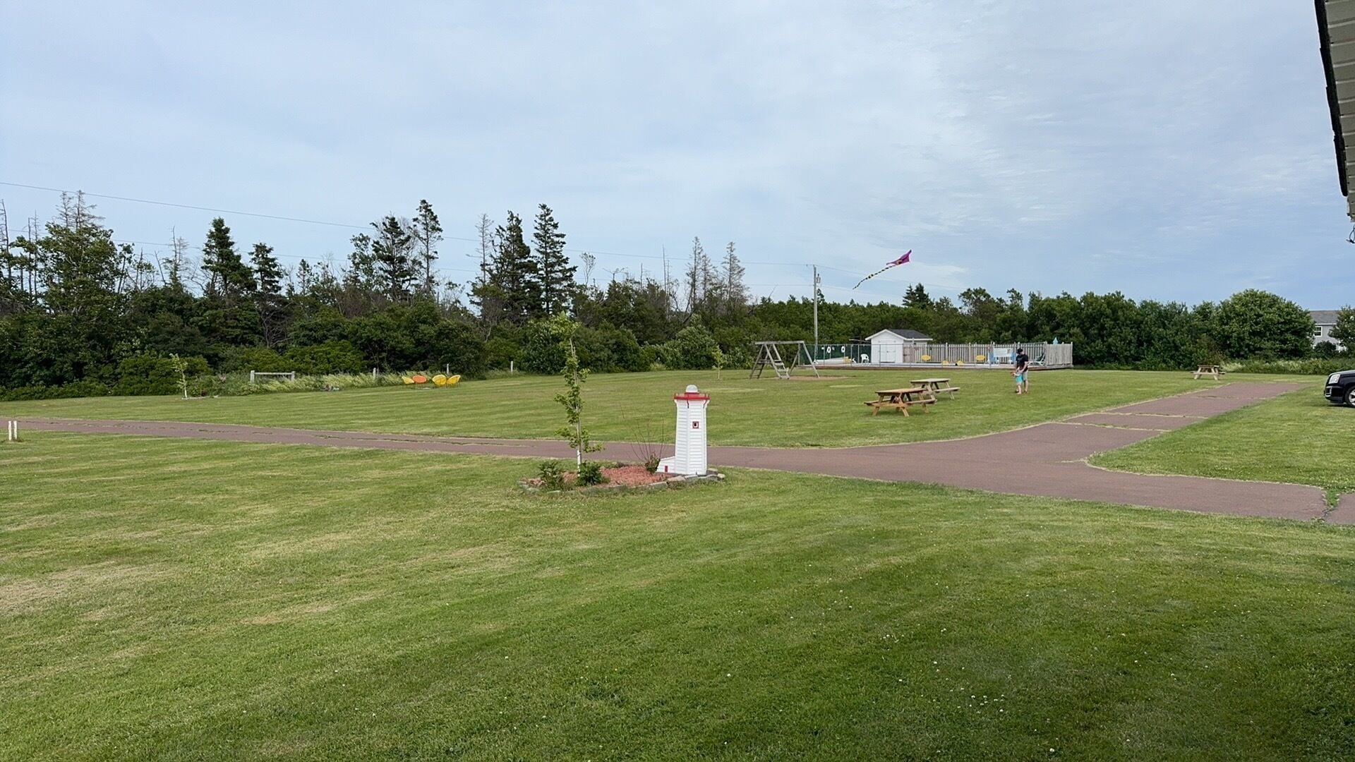 A grassy park area with picnic tables, a small white structure, and a playground.