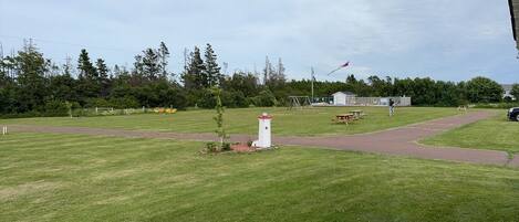 A grassy park area with picnic tables, a small white structure, and a playground.