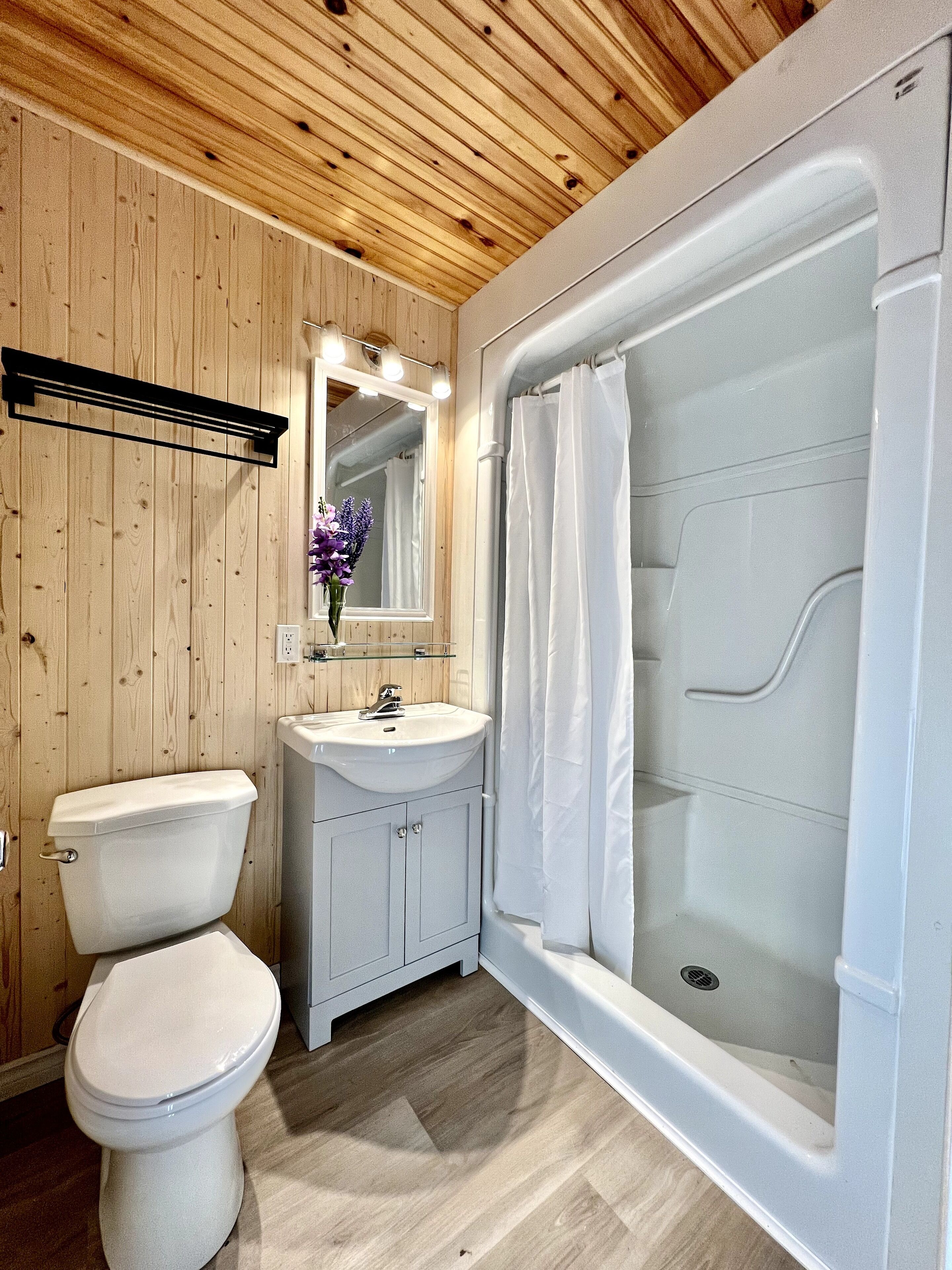 A bathroom with a wooden ceiling, a toilet, a sink with a mirror, and a glass-enclosed shower.