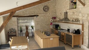 Una sala acogedora con sofá y una mesa de comedor, una cocina con estufa y alacenas, y una pared de piedra.