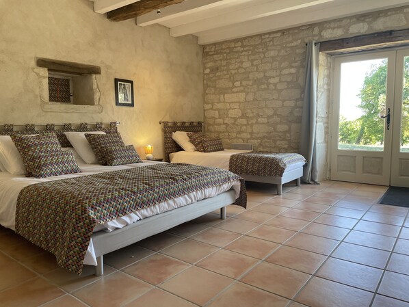 A bedroom with two beds, a stone wall, a wooden ceiling, and a view through a glass door.