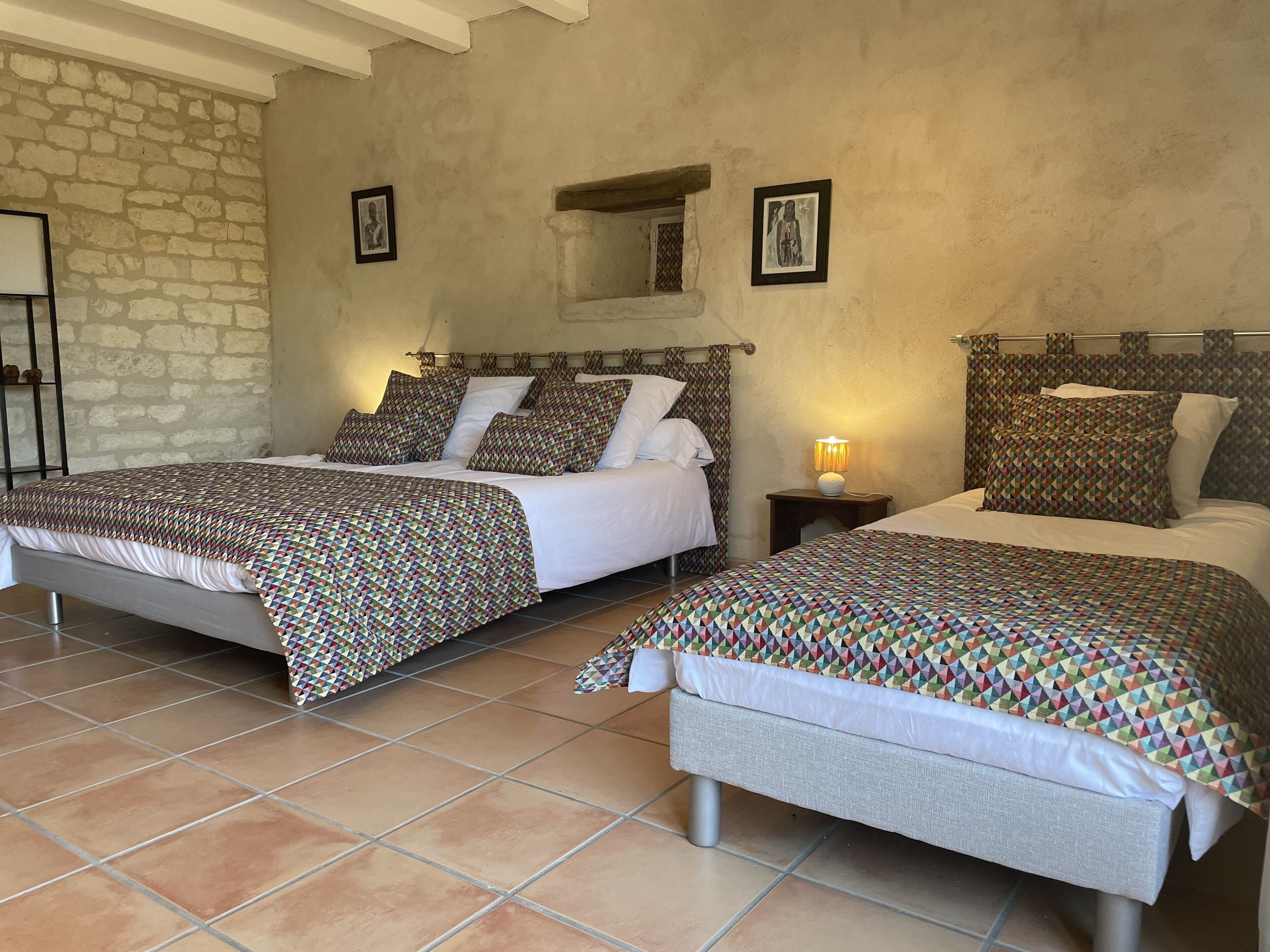 Une chambre double avec deux lits, chacun agrémenté de draps à motifs, un mur en pierre et une petite table de chevet avec une lampe.